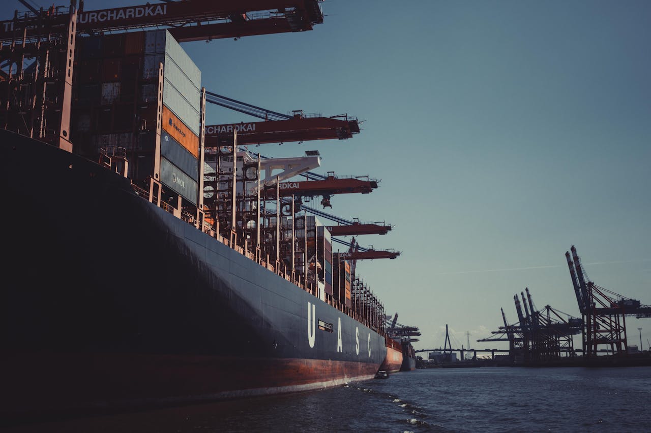 who-we-are A large cargo ship docked at Hamburg Harbor, cranes loading containers under a clear sky.